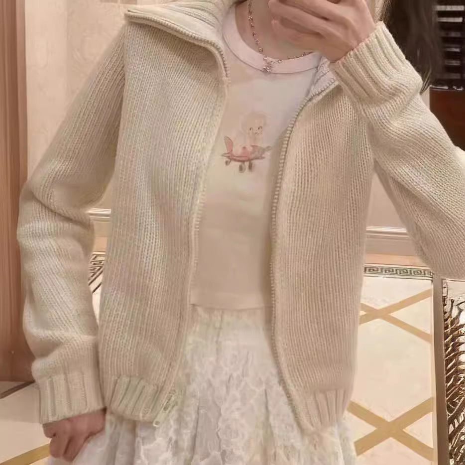 Cream knit zip cardigan worn open over a graphic tee and white lace skirt with ribbed cuffs