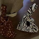 Brown spotted and black and white zebra triangle knot handle pouch bags side by side on a wooden table