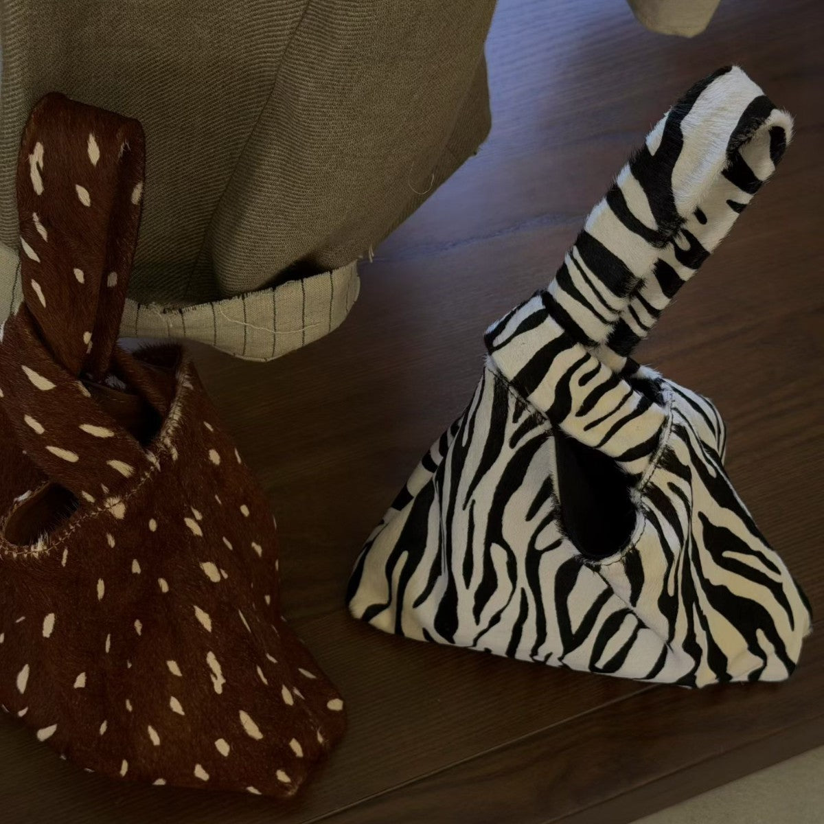 Brown spotted and black and white zebra triangle knot handle pouch bags side by side on a wooden table