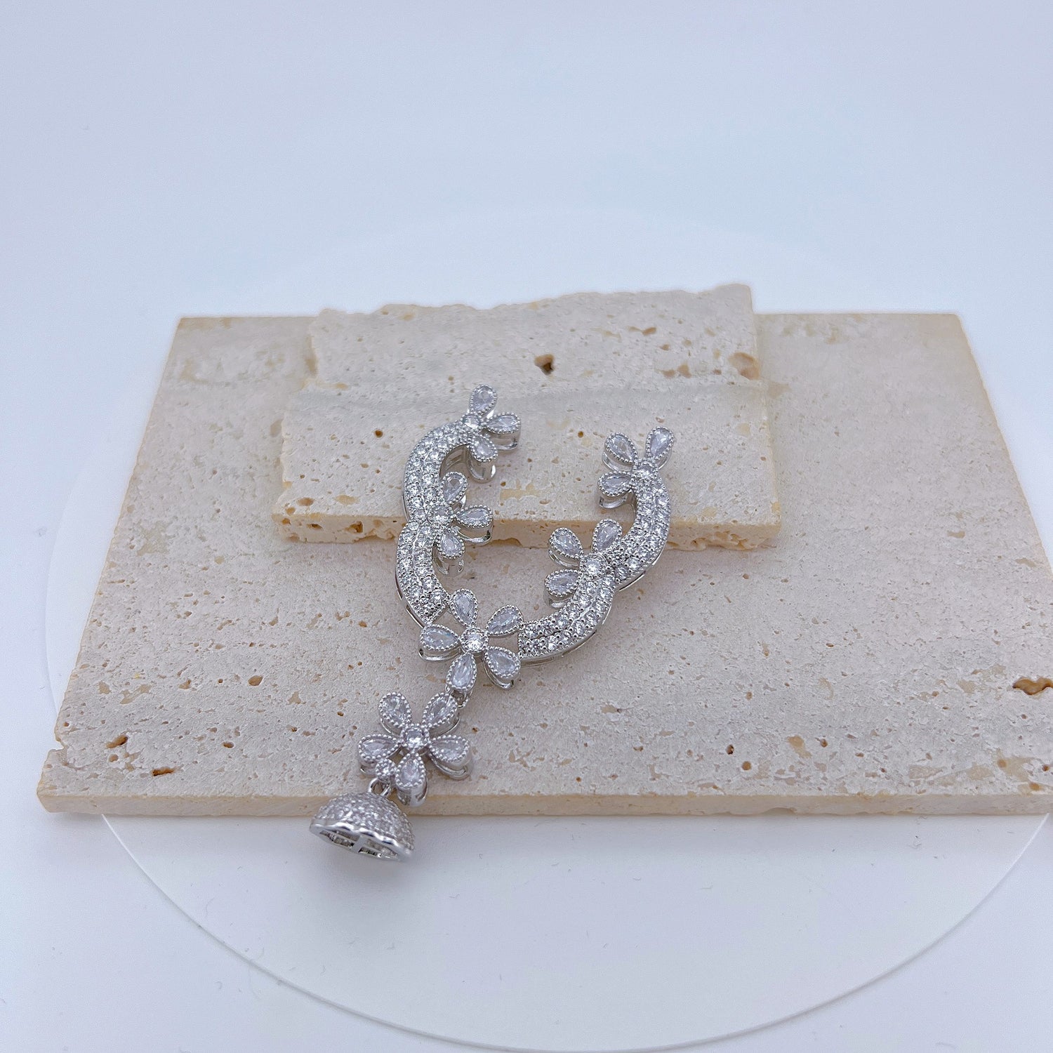 Close view of the connector finding, a floral scroll set with clear stones above a domed tassel cap