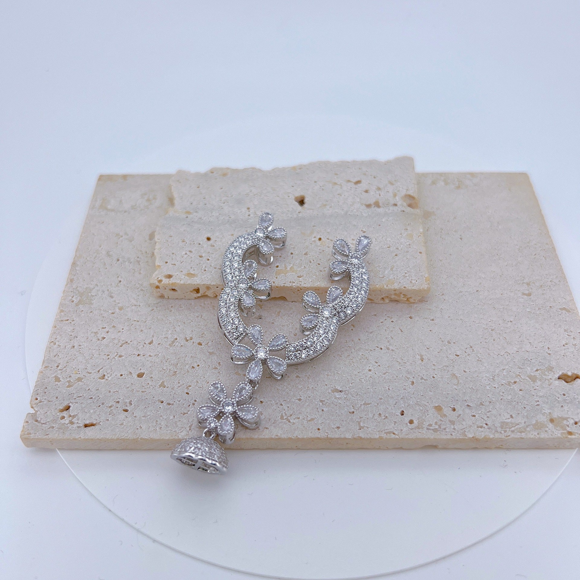 Close view of the connector finding, a floral scroll set with clear stones above a domed tassel cap