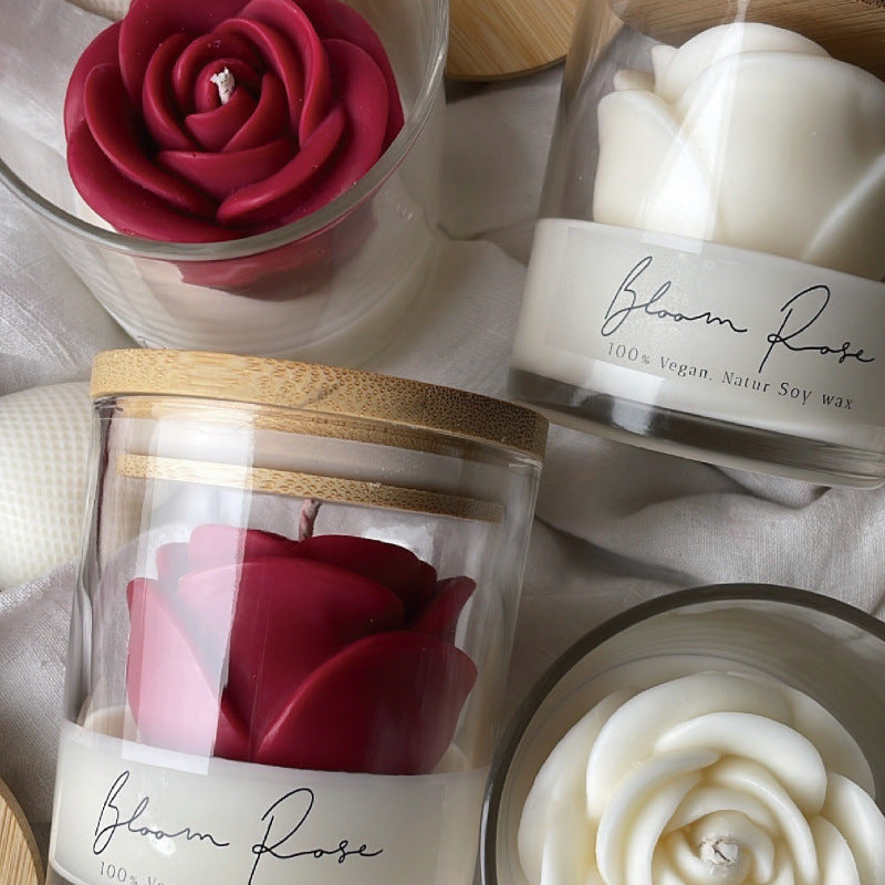 Red rose candle in a glass jar with a bamboo lid beside white rose candles on a linen cloth