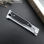 Closed folding pocket knife with a silver aluminum frame and black textured insert panel on a black leather surface