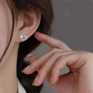 Saturn planet stud earring worn on the ear, pale blue opalescent stone glowing within a silver-tone orbit