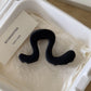 Matte black large wavy acrylic hair claw clip lying on cream tissue in the box