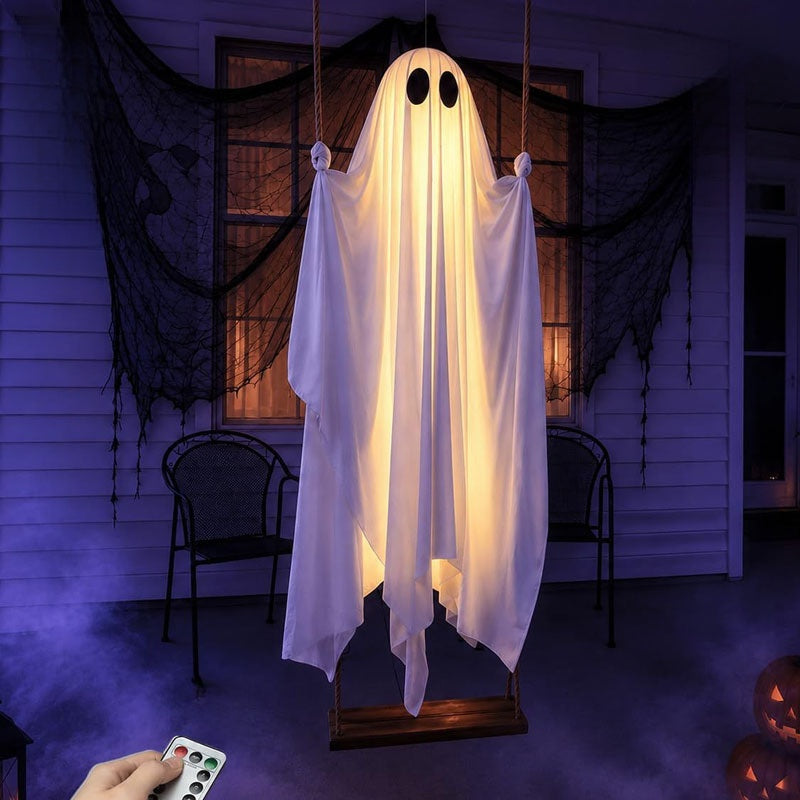 Hand holding the remote control in front of a lit ghost swing decoration on a dark porch