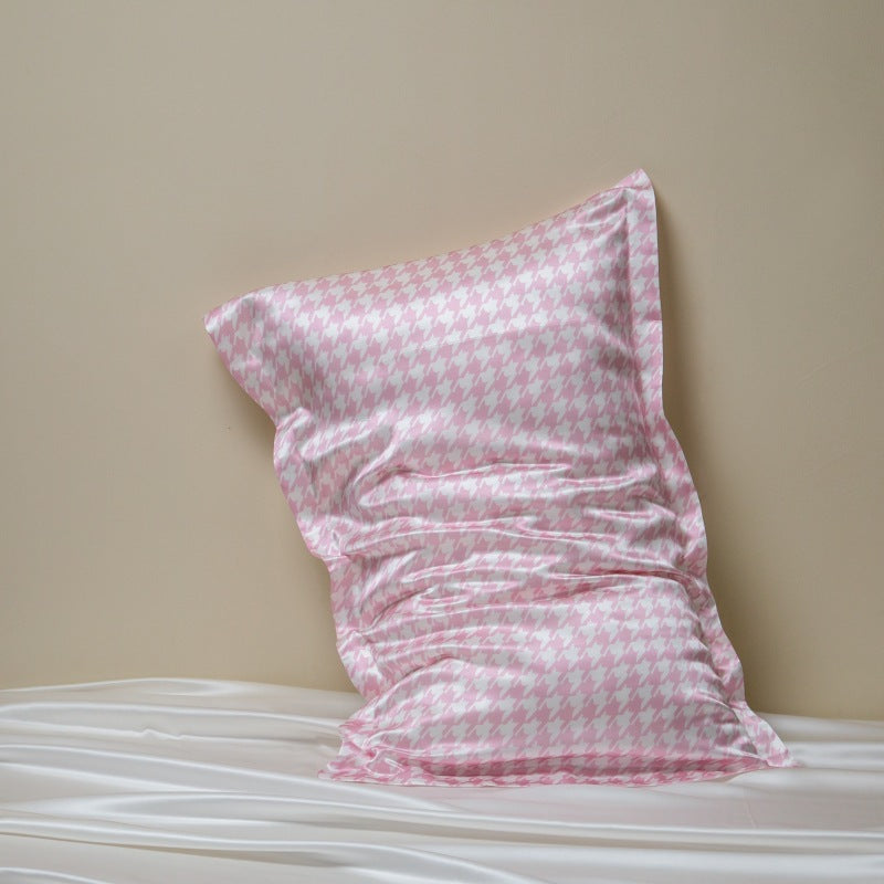Pink and white houndstooth silk pillowcase leaning on a beige wall above white silk