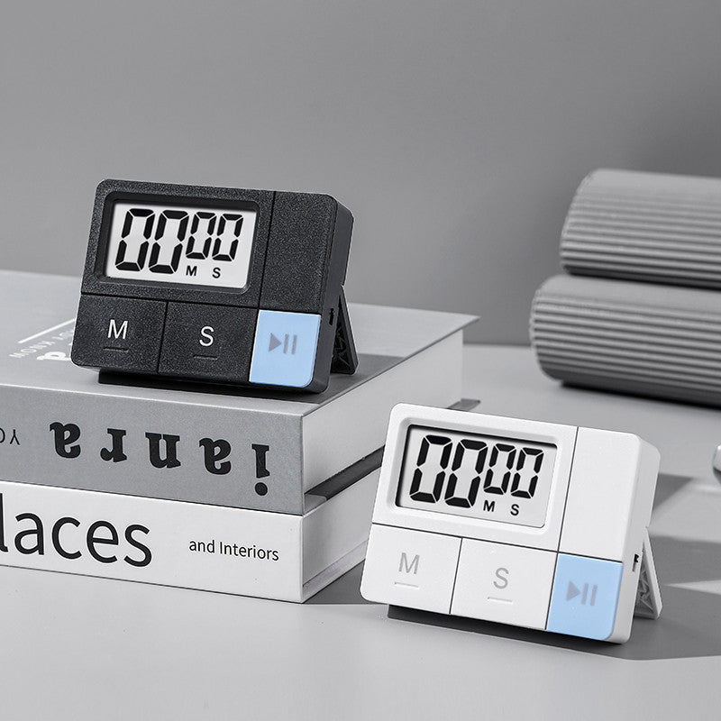 Black and white plastic digital timers displayed on stacked books in a styled interior scene