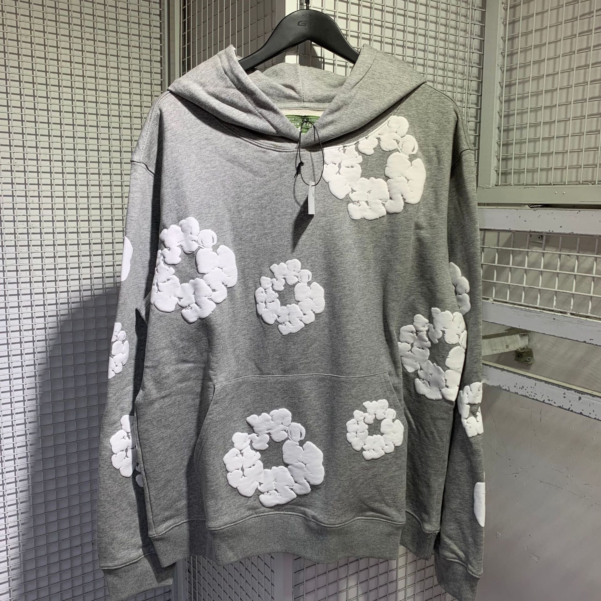 Grey cotton wreath print hoodie on a hanger showing the front pocket and hood