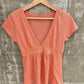Orange short-sleeve deep V-neck top with an empire waist band and gathered hem on a wooden hanger