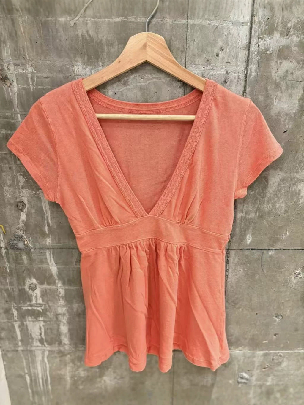Orange short-sleeve deep V-neck top with an empire waist band and gathered hem on a wooden hanger