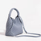 Grey woven bucket bag with the slim adjustable crossbody strap clipped on and extended to the side