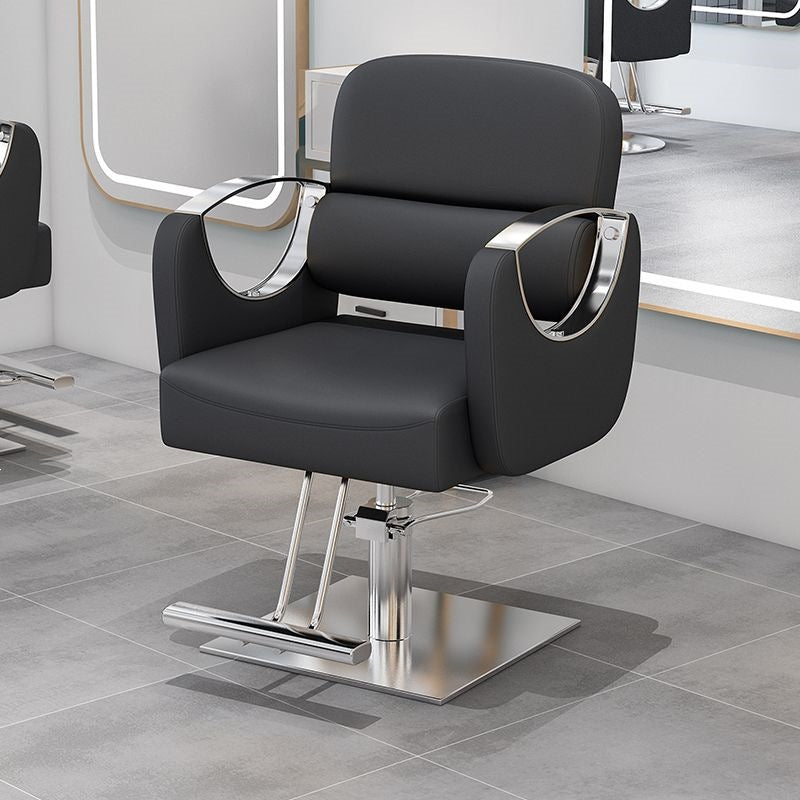 Gray salon styling chair with curved silver armrests on a silver disc base in a salon