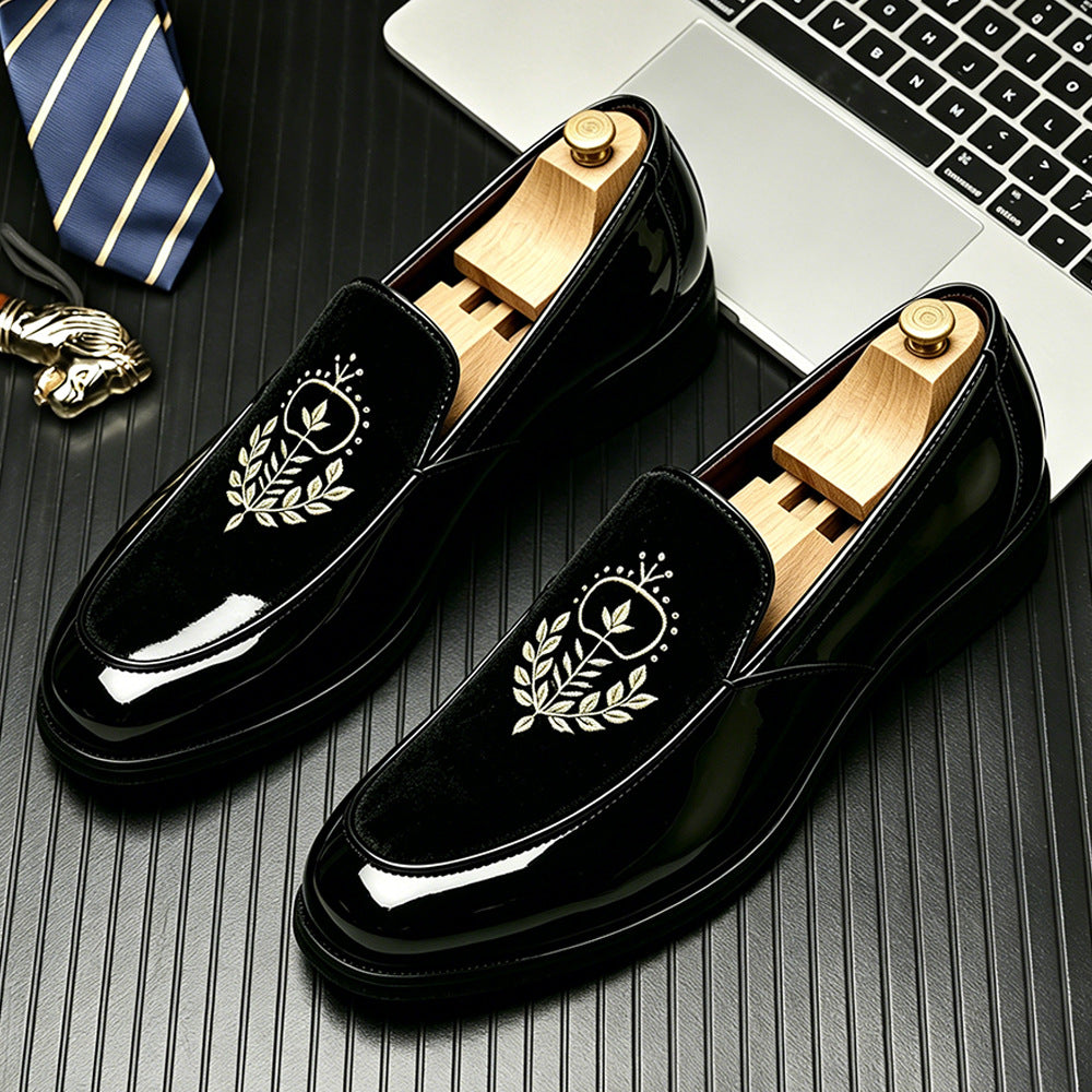 Glossy black loafers with a black velvet vamp and an embroidered laurel crest on a desk with a tie, size 44 option