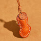 Close view of the tan orange peanut leather pendant with stamped tag, glass fruit bead and cream stitching