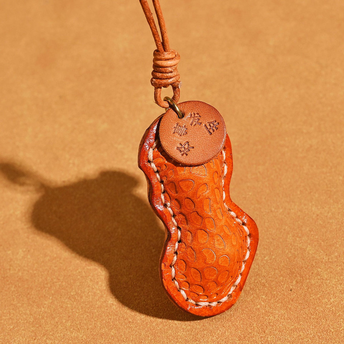 Close view of the tan orange peanut leather pendant with stamped tag, glass fruit bead and cream stitching