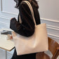 Woman wearing a cream PU tote on her shoulder with a black blazer, seated at a small cafe table
