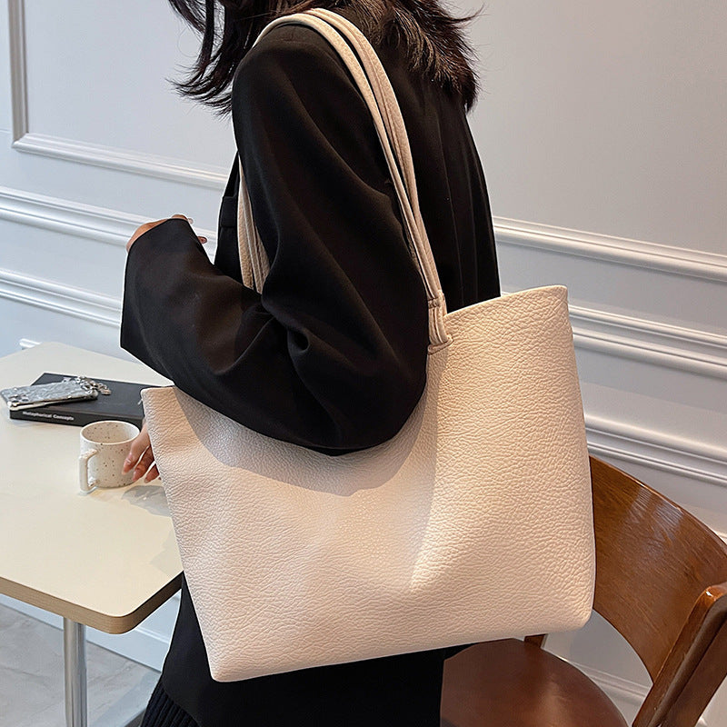 Woman wearing a cream PU tote on her shoulder with a black blazer, seated at a small cafe table