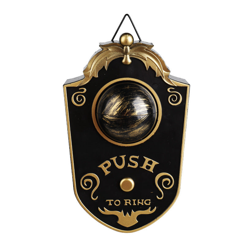 Black and gold Halloween eyeball doorbell prop hanging by its wire hook, glowing green eye and Push To Ring
