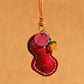 Close view of the red peanut leather pendant with cream stitching, stamped tag and orange glass fruit bead, red option
