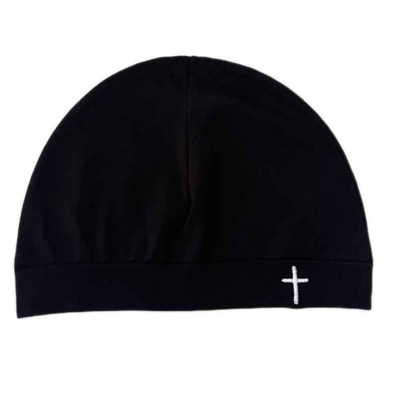 Close fitting dome beanie worn low over the ears, embroidered cross on the front