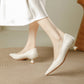 Cream pointed toe pumps with a low flared heel worn with a white skirt on a woven rug