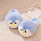 Pair of blue plush penguin slippers with yellow beaks and black eyes on a beige rug beside a newspaper, Blue Open-Heel