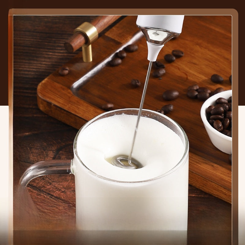 Handheld frother whipping milk into thick foam inside a glass coffee cup