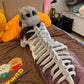 The grey dinosaur skeleton plush hood laid flat, showing the skull and segmented spine