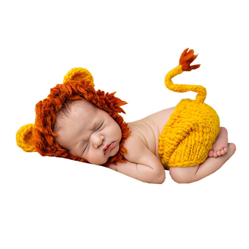 Sleeping newborn in the orange knit lion bonnet and shorts on a white background