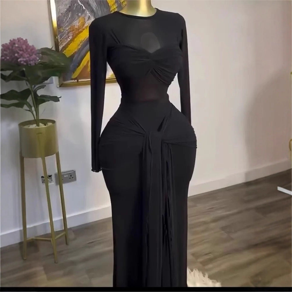 Black long sleeve maxi dress on a mannequin with twisted bust band and draped front tie beside a plant