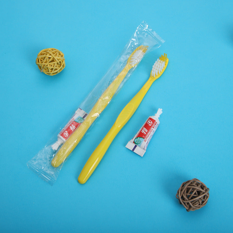 Yellow plastic toothbrush with a small toothpaste tube and clear wrap on a blue background