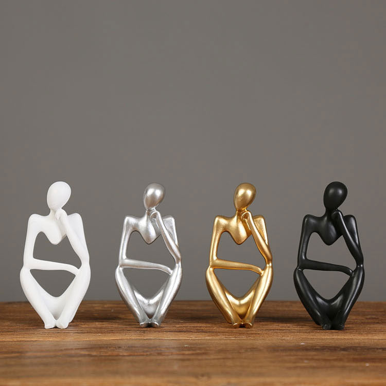 Row of abstract resin meditator figurines in white, gold and black finishes on a wooden shelf