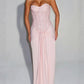 Woman in a pink strapless long dress with a sequin bodice and draped hip knot on a grey background