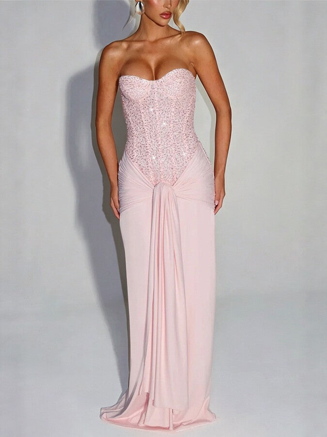 Woman in a pink strapless long dress with a sequin bodice and draped hip knot on a grey background