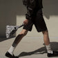 Person walking and carrying the zebra stripe triangle pouch bag by its handle, wearing black shorts and loafers