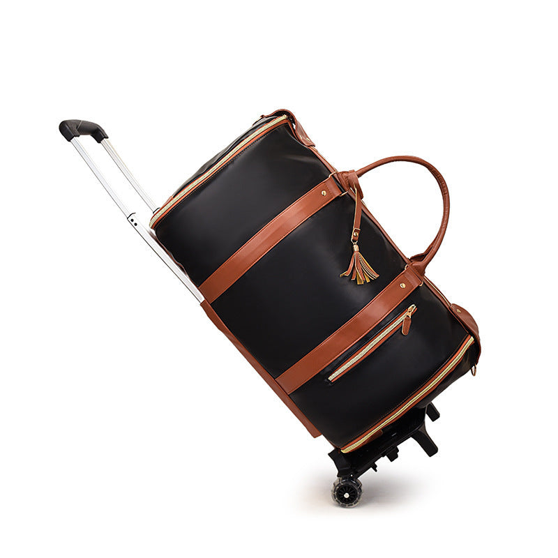 Black duffel travel bag with brown straps, a gold toned zip, a tassel, a pull rod and two wheels