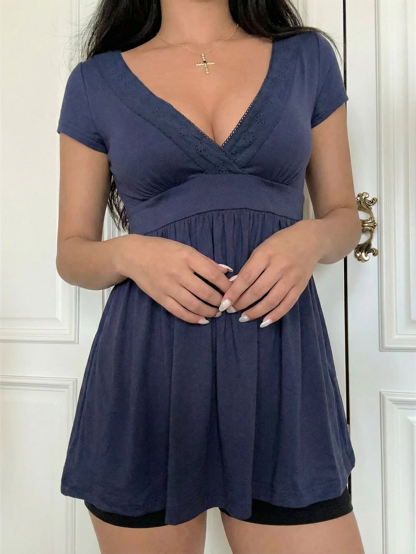 Model in the navy V-neck babydoll top with eyelet lace trim and a gathered peplum hem