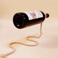 Cream rope bottle holder with a wine bottle seen from its base end, held level above a beige surface, cream not offered