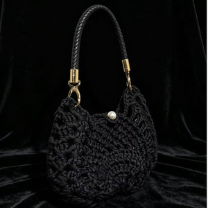 Black handwoven wool bag with braided black handle and pearl-white button against black velvet