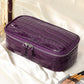 Purple crocodile pattern leather cosmetic bag on cream satin beside makeup brushes and a palette