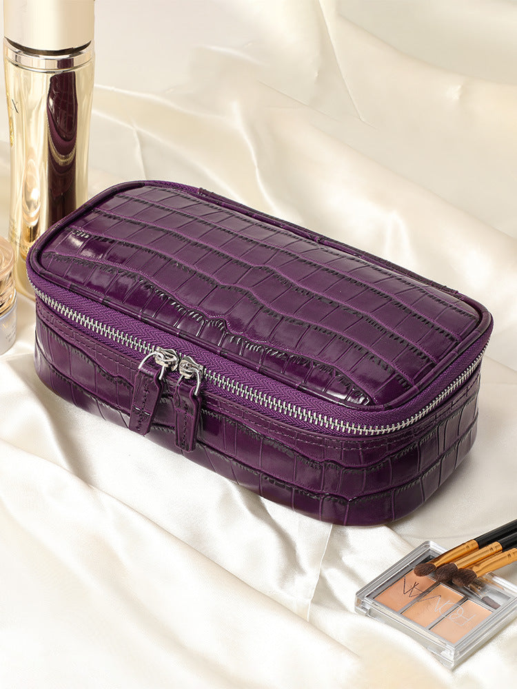Purple crocodile pattern leather cosmetic bag on cream satin beside makeup brushes and a palette