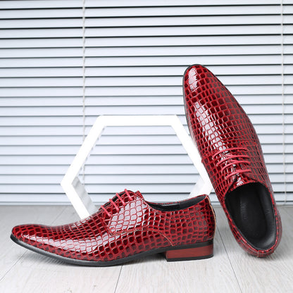 Pair of red croc embossed derby shoes with pointed toes, one leaning on a white hexagon, striped studio wall behind