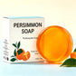Amber persimmon soap bar in front of a Persimmon Soap box on a pale blue and white background with leaves