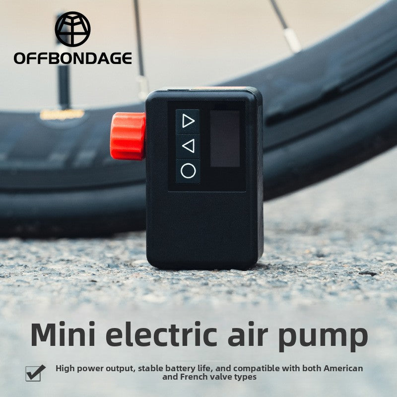 Black mini electric air pump with red knob, three buttons and LED screen standing on gravel in front of a bicycle tire