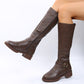 Brown vegan leather knee high riding boots on a model with side zipper, ankle buckle strap and ridged sole