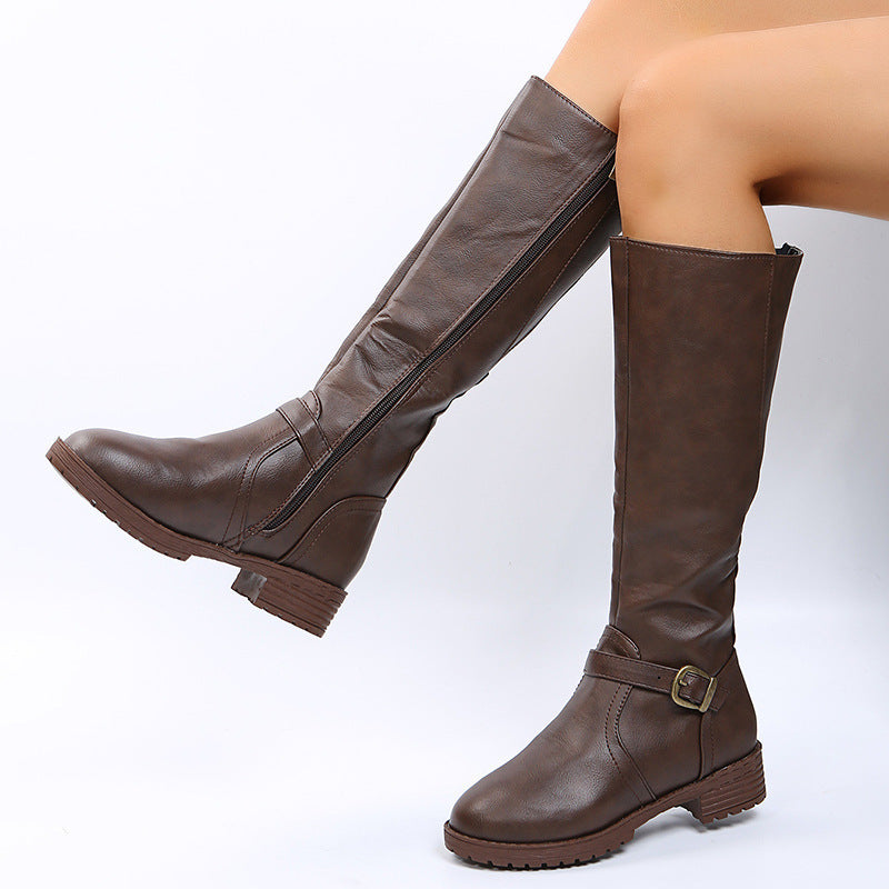 Brown vegan leather knee high riding boots on a model with side zipper, ankle buckle strap and ridged sole