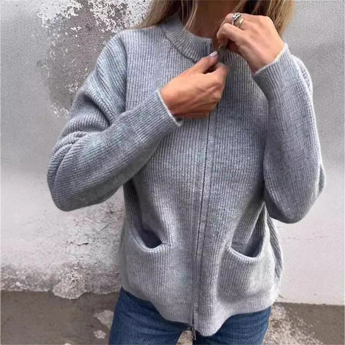 Woman zipping a gray ribbed knit cardigan at the neck, patch pockets visible