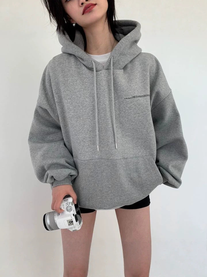 Light gray oversized hooded sweatshirt with drawstrings and a front pouch pocket, a camera held in one hand
