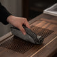 Hand wiping a dark gray tea cloth across a slatted wooden tea tray with the pile side showing